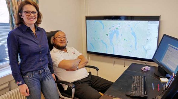 Sonja og Kenneth hos AEX er fornøyde foran webportalen som henger i storskjerm på veggen